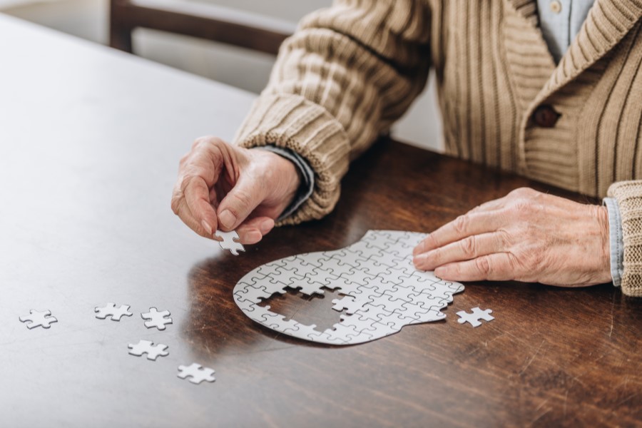 Mężczyzna chorujący na chorobę Parkinsona układa puzzle o kształcie głowy widzianej z profilu.