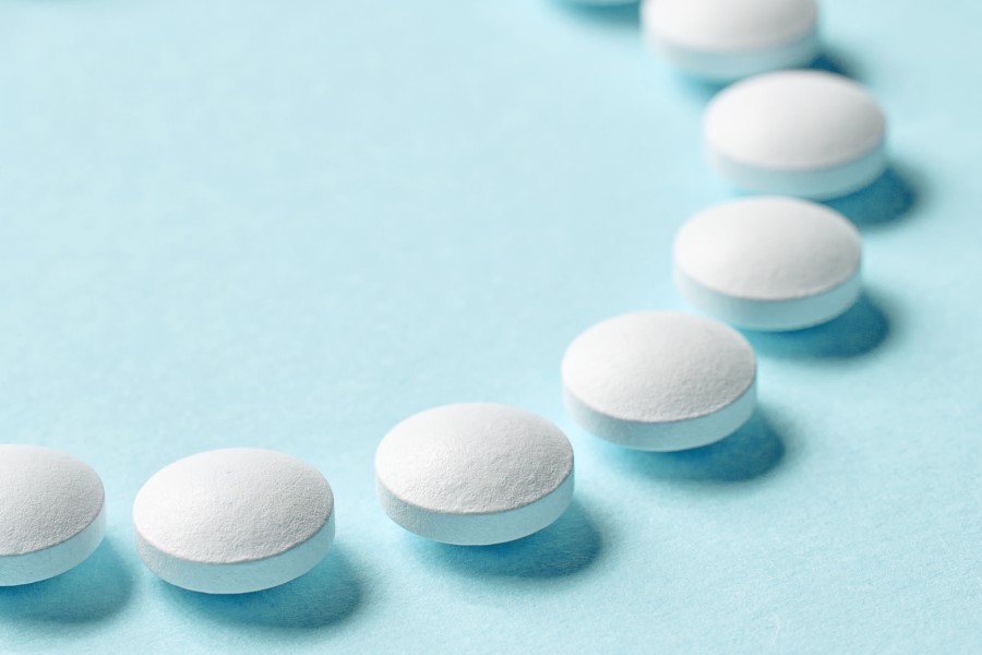 Białe tabletki ułożone na błękitnym tle.