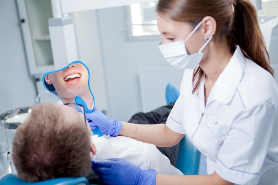 Pacjent u stomatologa, po piaskowaniu zębów ogląda efekty czyszczenia w lusterku.