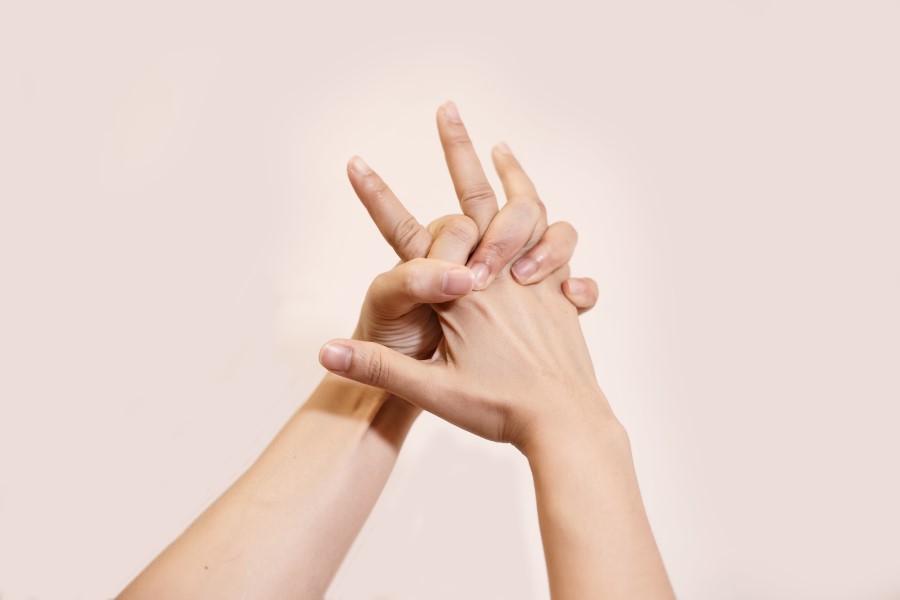 Kobiece dłonie splecione na różowym tle. Przestrzeń między palcami swędzi z powodu potnicy dłoni.