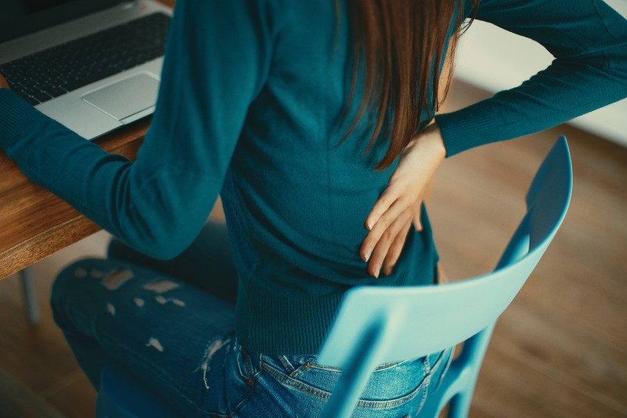 Kobieta siedzi przy biurku, odczuwa ból w dolnym odcinku kręgosłupa.