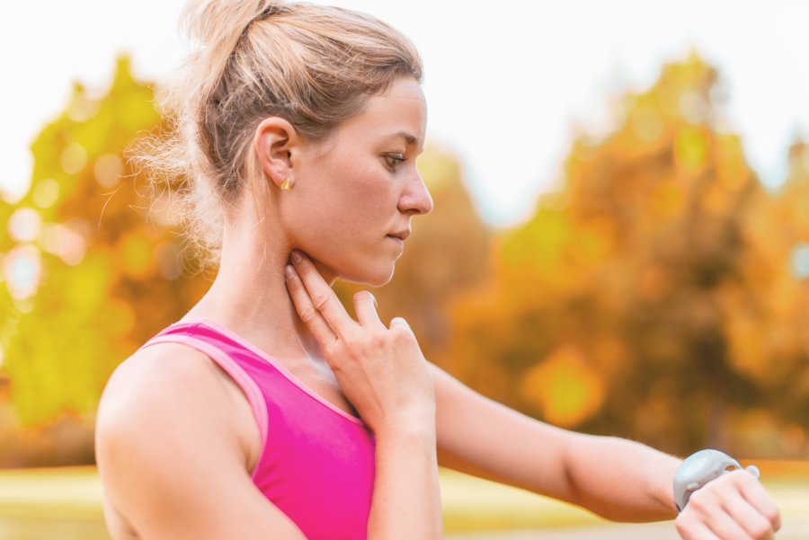 Ubrana na sportowo kobieta przed biegiem w parku mierzy swoje tętno spoczynkowe na tętnicy szyjnej.