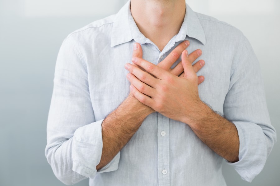 Mężczyzna w białej koszuli, jego dłonie są skrzyżowane na klatce piersiowej, w okolicy serca.