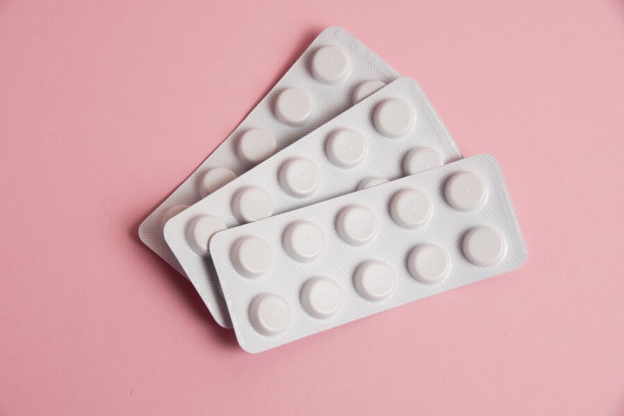 Trzy blistry tabletek na różowym tle.