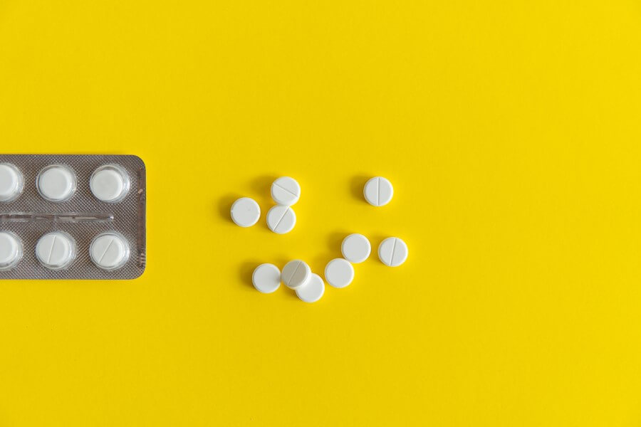 Blister oraz białe tabletki leżące na żółtym tle.
