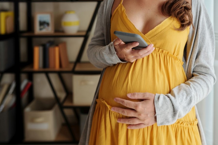 Ciężarna kobieta sprawdza na telefonie wyniki badań prenatalnych.
