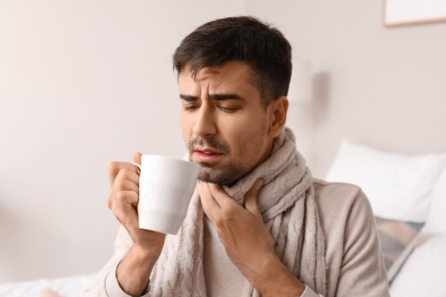 Przeziębionego mężczyznę boli gardło przy przełykaniu ulubionej herbaty.