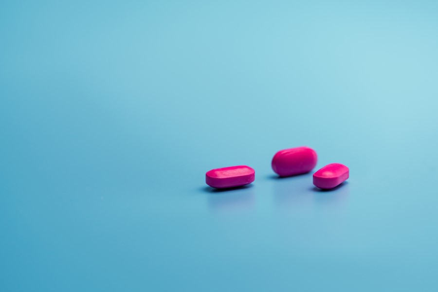 Różowe tabletki na turkusowym tle, zawierające ibuprofen.