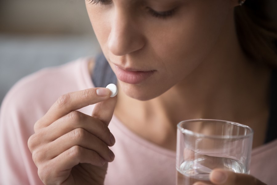 Kobieta zażywa tabletkę aspiryny (kwasu acetylosalicylowego), którą popije szklanką wody.