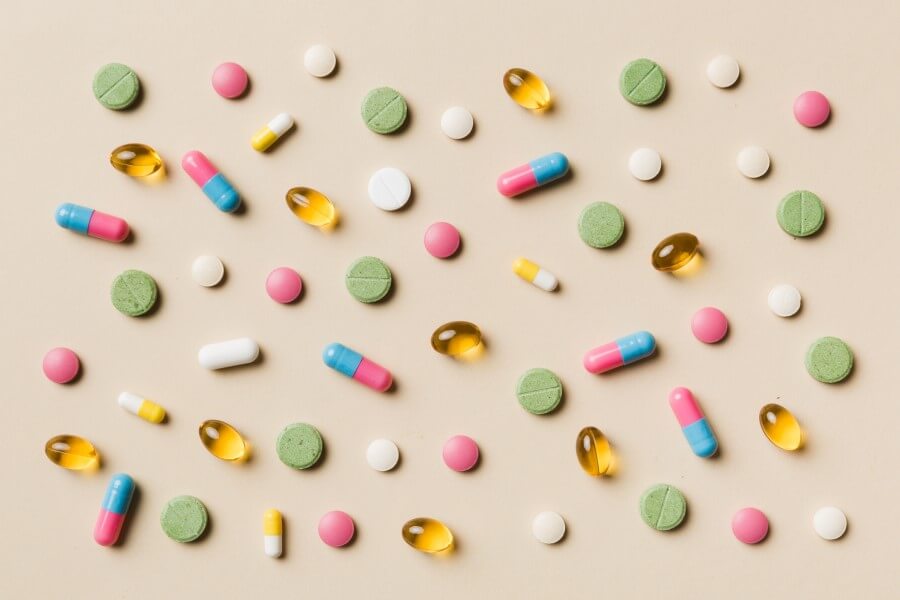 Kolorowe tabletki i kapsułki rozsypane na pastelowym tle.
