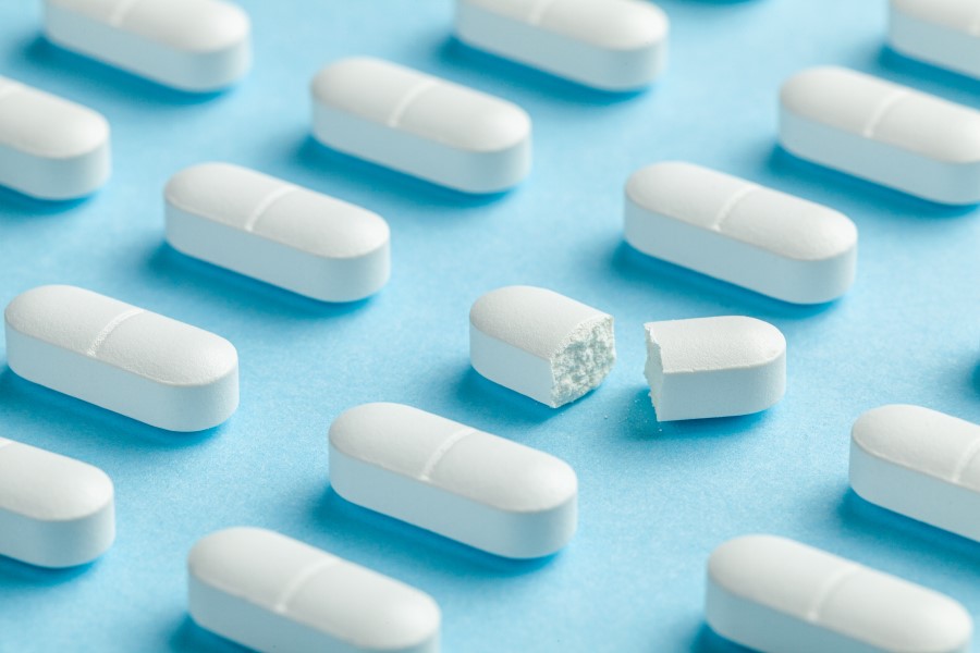 Białe tabletki z podziałką ułożone w równych rzędach. Jedna z tabletek jest przełamana.