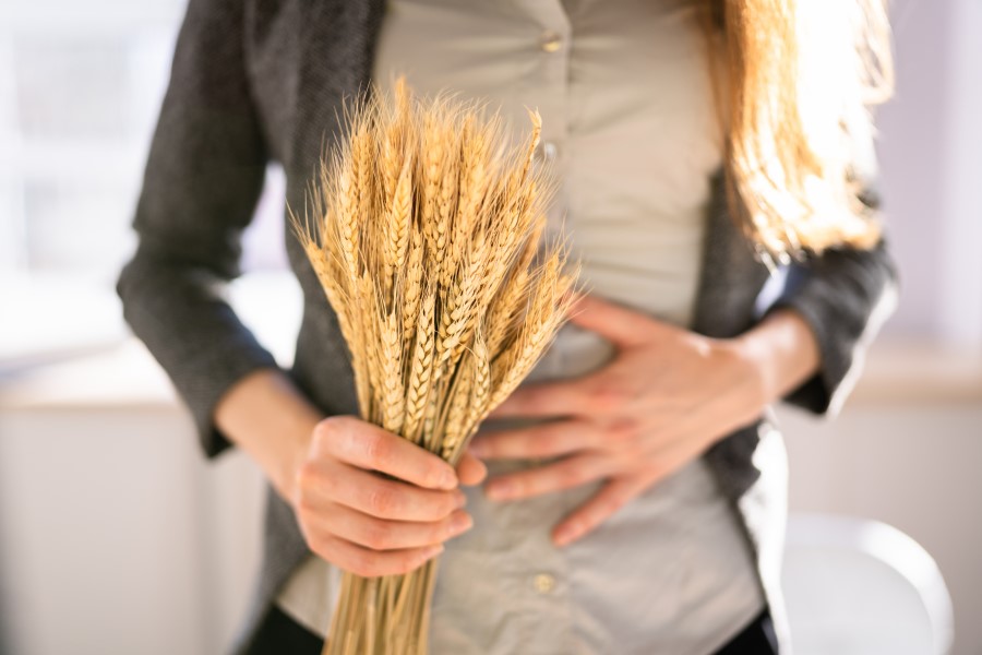 Kobieta trzyma w ręce kłosy pszenicy, cierpi na nietolerancję glutenu.