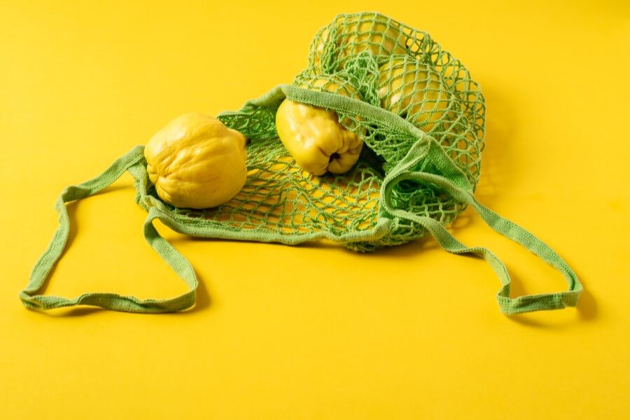 Żółte tło. Owoce pigwy wysypujące się z zielonej, siateczkowej torby na zakupy.