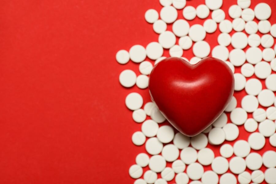 Białe tabletki na czerwonym tle. Na tabletkach leży czerwona figurka serca.