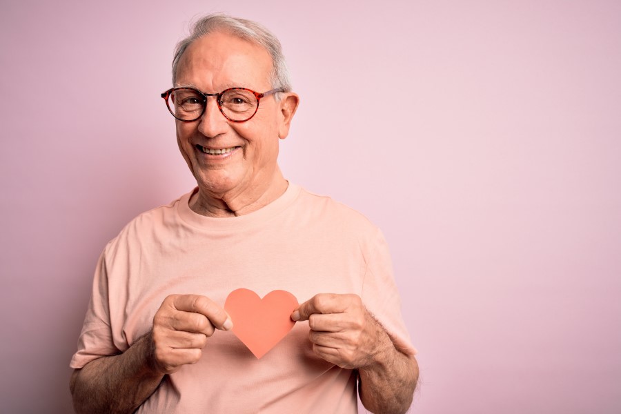 Starszy mężczyzna trzyma na wysokości klatki piersiowej wycięte z papieru serce.