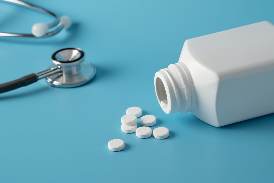 Buteleczka leków i tabletki rozsypane na niebieskim tle. W lewym górnym roku lekarski stetoskop.