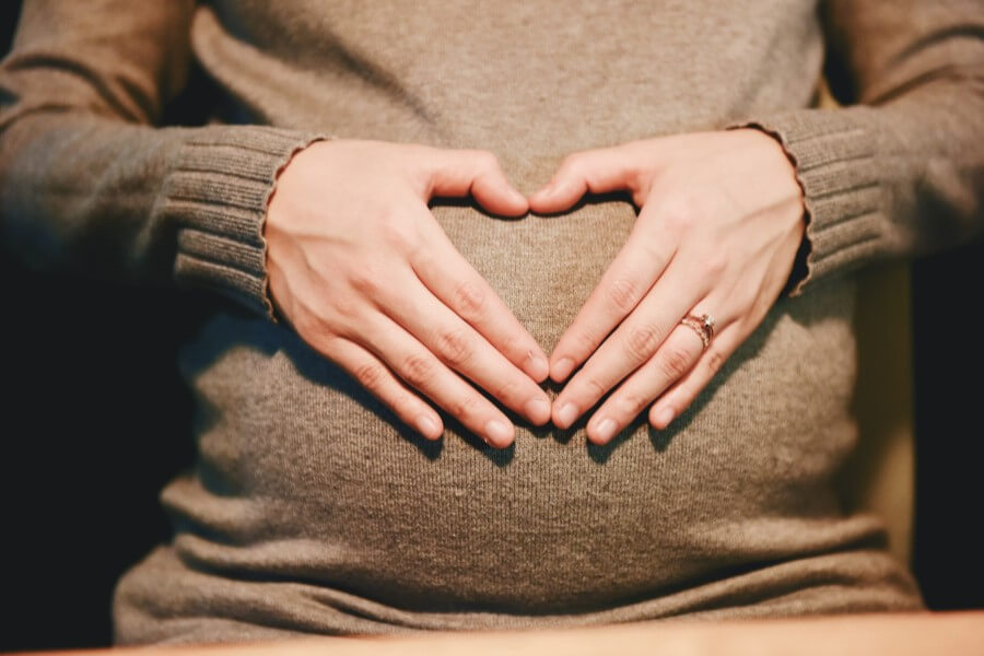 Kobieta trzyma dłonie na ciążowym brzuchu, układa je w kształt serca.