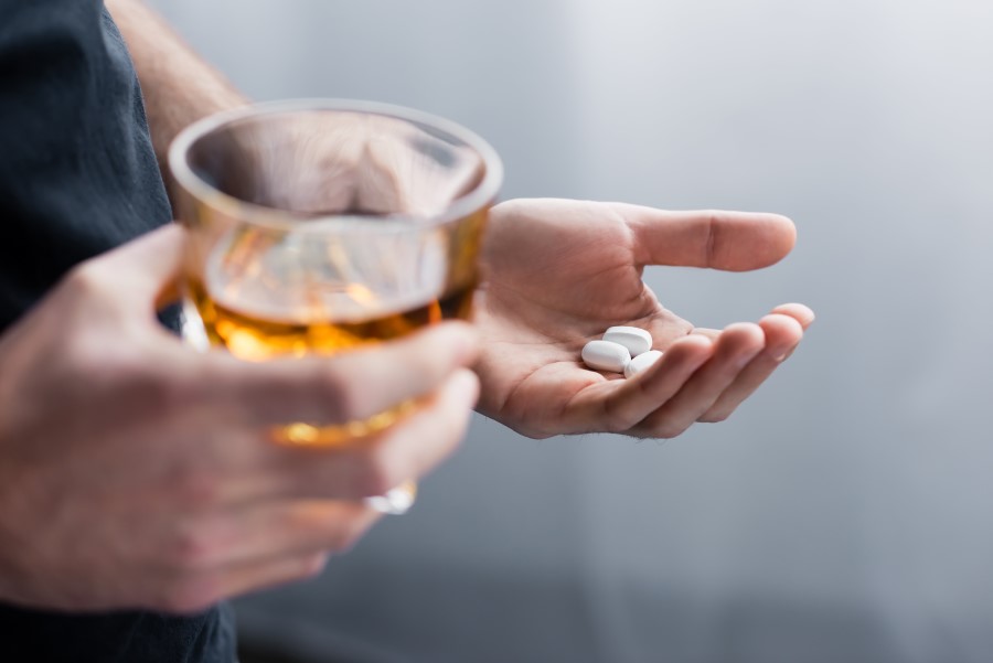 Mężczyzna trzyma w jednej dłoni alkohol w szklance, w drugiej tabletki.
