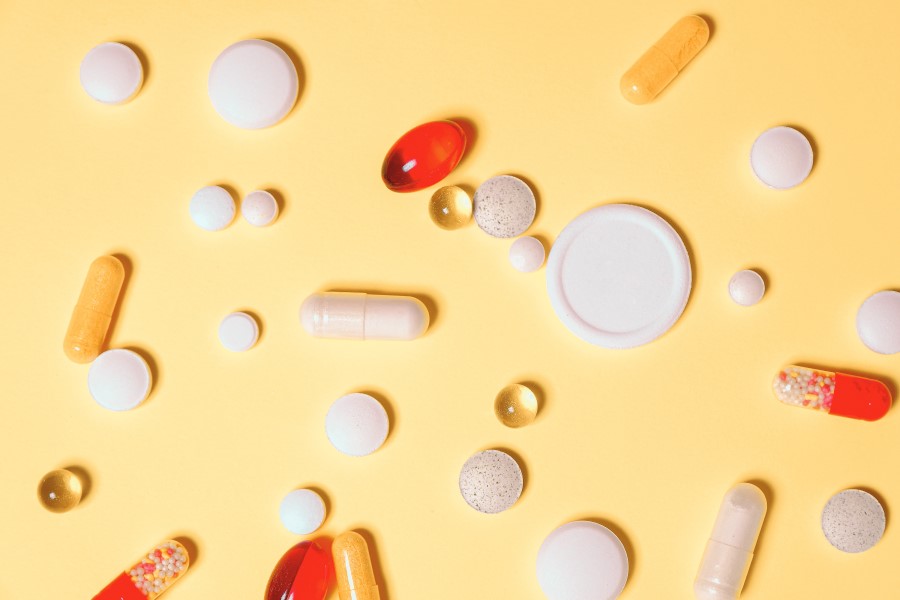 Kapsułki i tabletki leków na żółtym tle.