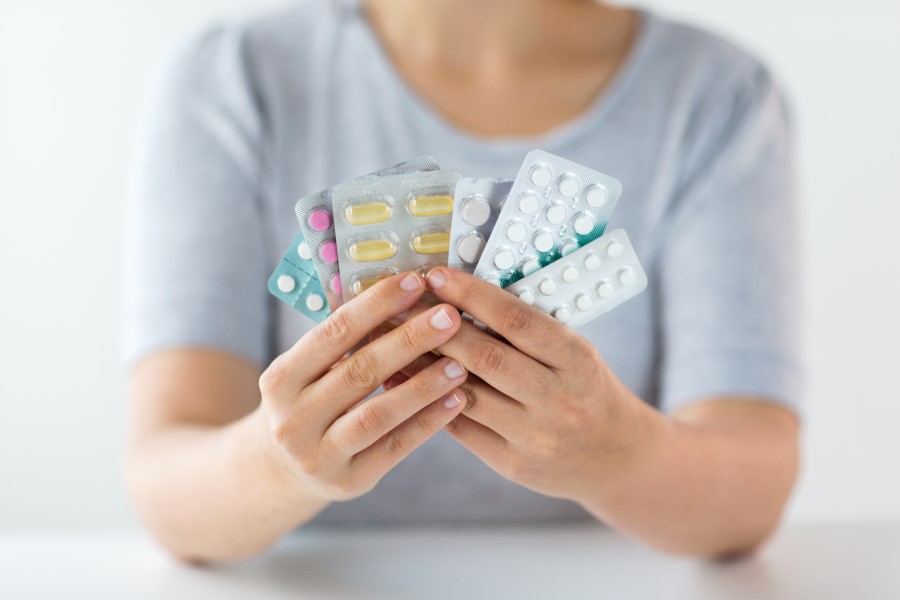 Kobieta trzyma w dłoniach kilka blistrów różnych leków.