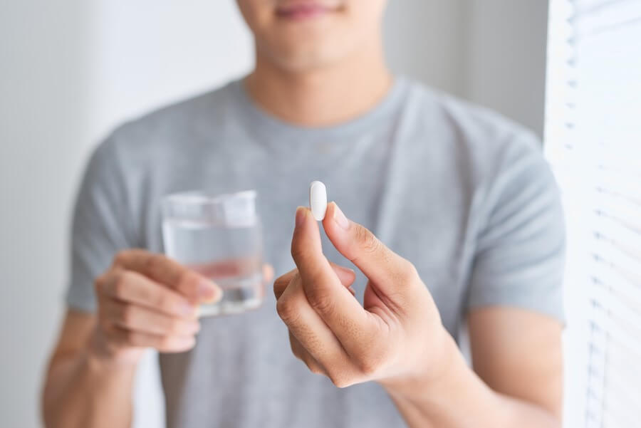 Mężczyzna trzyma szklankę wody i tabletkę paracetamolu.
