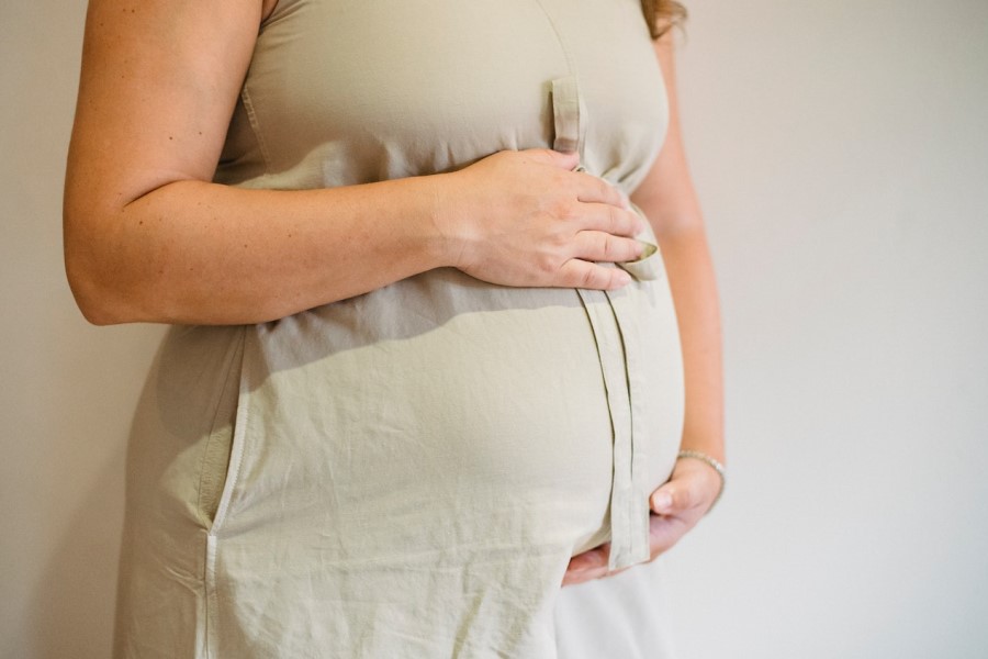 Kobieta w zaawansowanej ciąży trzyma się za ciążowy brzuszek.