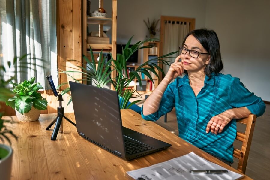 Kobieta w okularach siedzi przy stole, korzysta z laptopa podczas pracy.