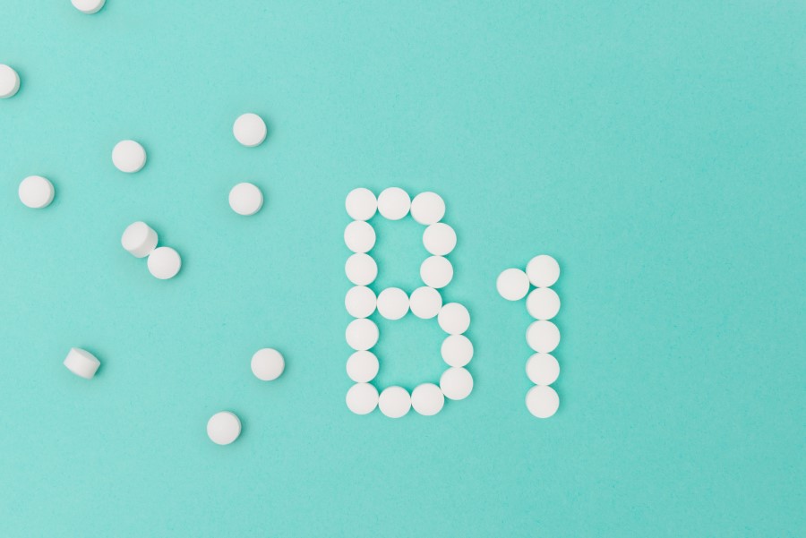 Białe tabletki na niebieskim tle, ułożone w nazwę witaminy B1.