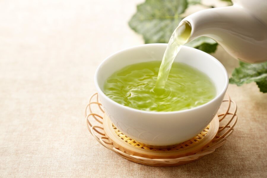 Zielona herbata nalewana z czajniczka do ceramicznej czarki, na wiklinowej podstawce.